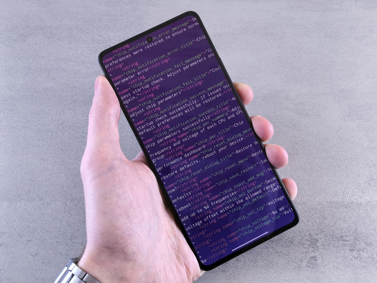 hero-02 Close-up of a smartphone displaying code text held in a person's hand.